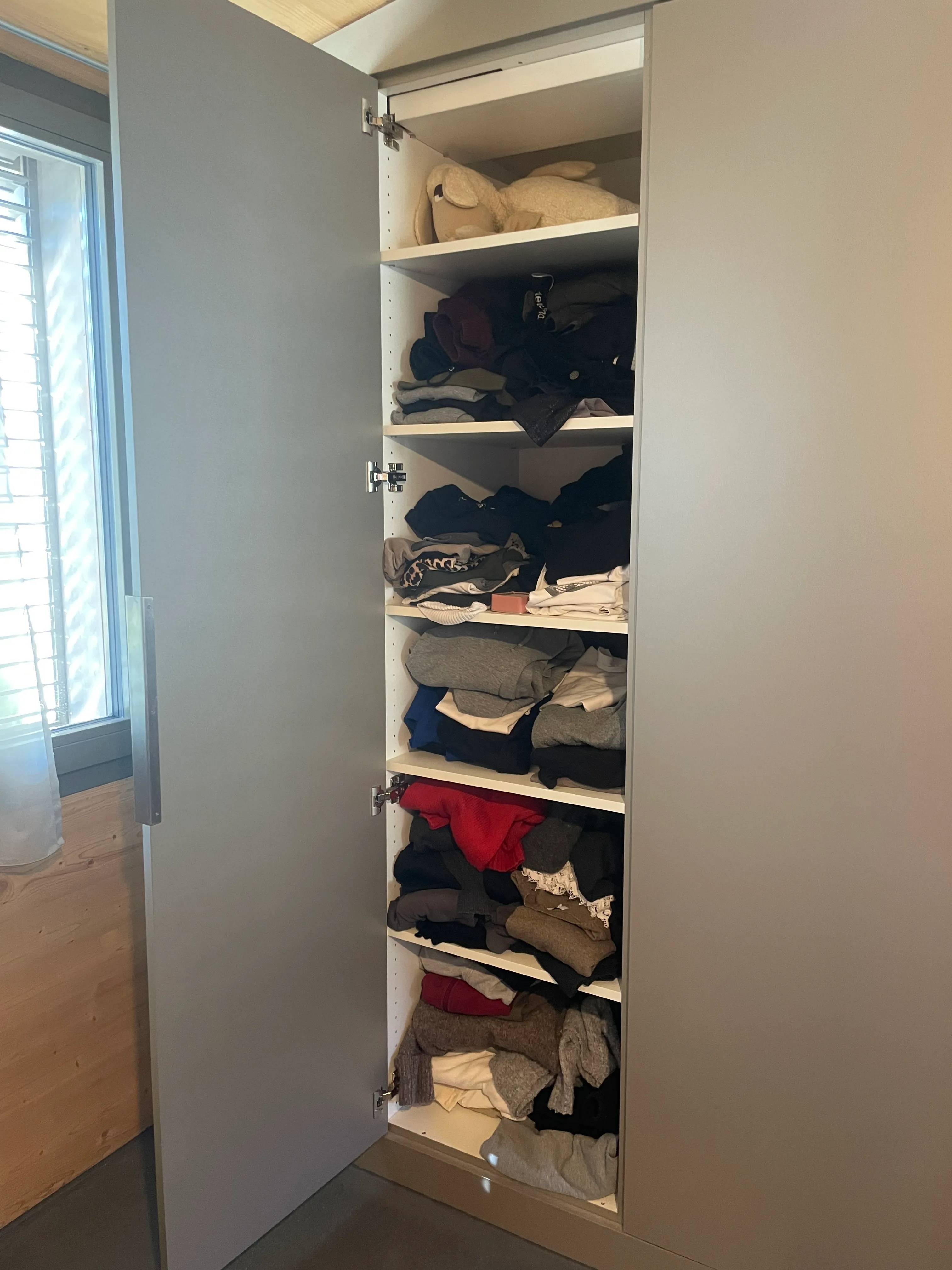 Offener kleiner Kleiderschrank, Fächer überfüllt.